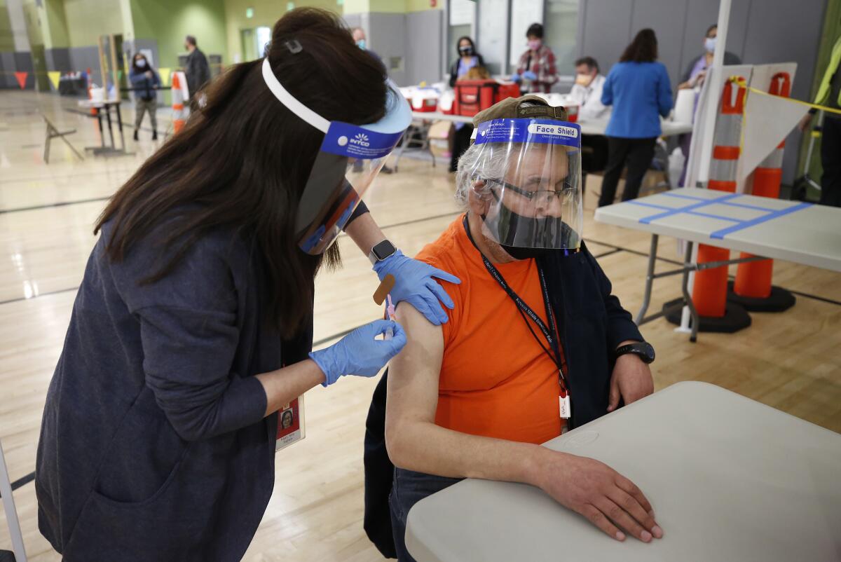 A woman holds a hypodermic needle to a man's arm