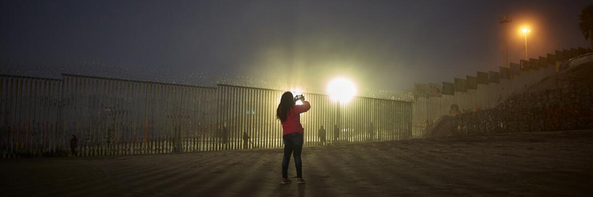 A woman uses her phone to record the border wall along the beach in Tijuanao.