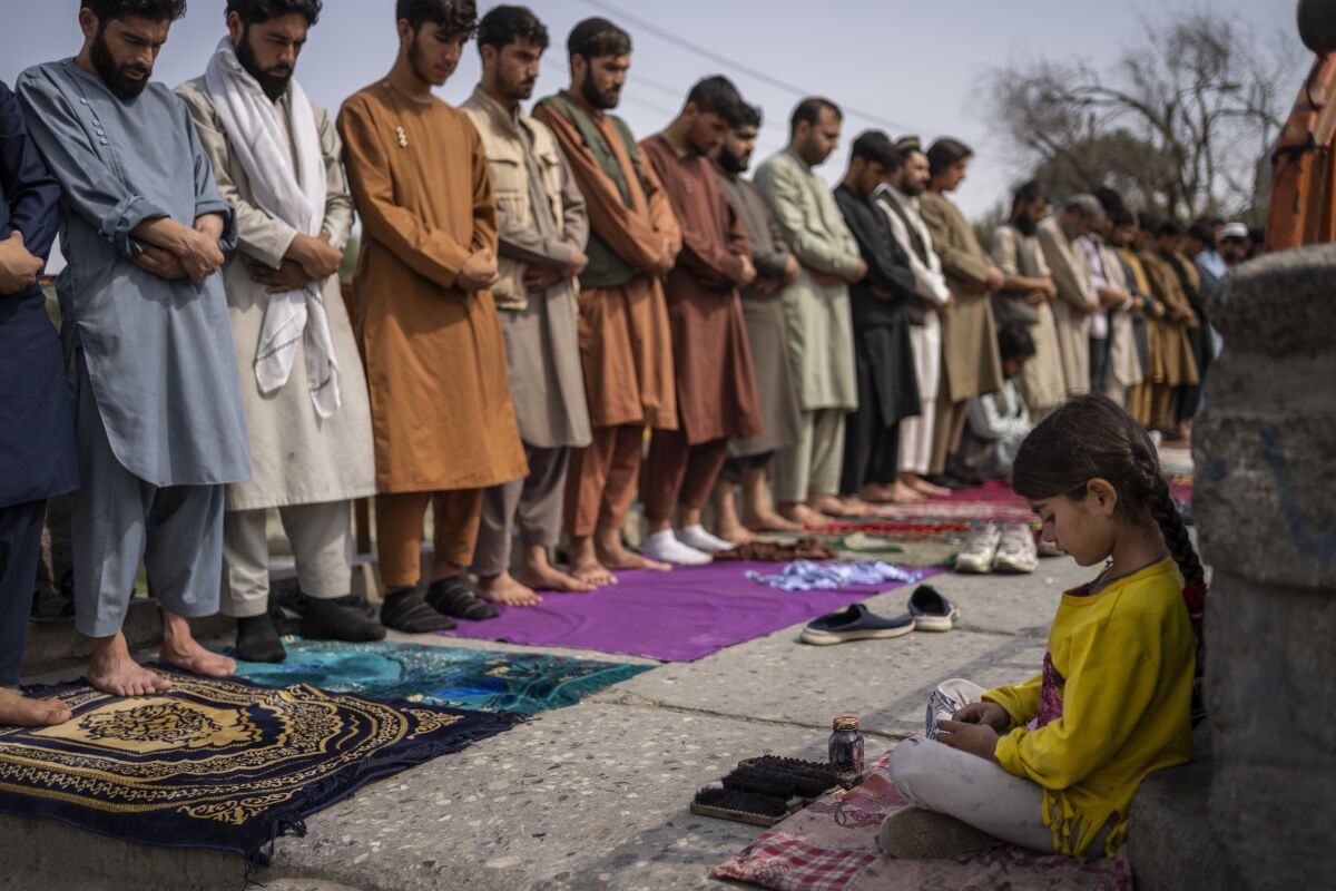 An Afghan girl sits in the street while men pray.