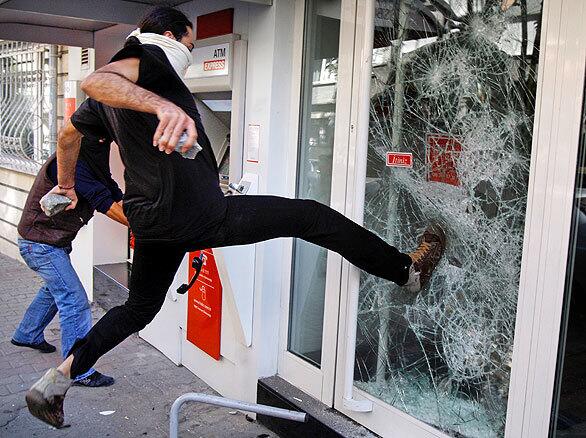 A masked man attacks the office of a foreign bank as demonstrators roam the streets of Istanbul, protesting the International Monetary Fund and the World Bank, which are holding an annual meeting in the city. Protesters clashed with police who used tear gas and water cannons to disperse demonstrators who attacked several bank offices and business in Istanbul, for the second day of protests.