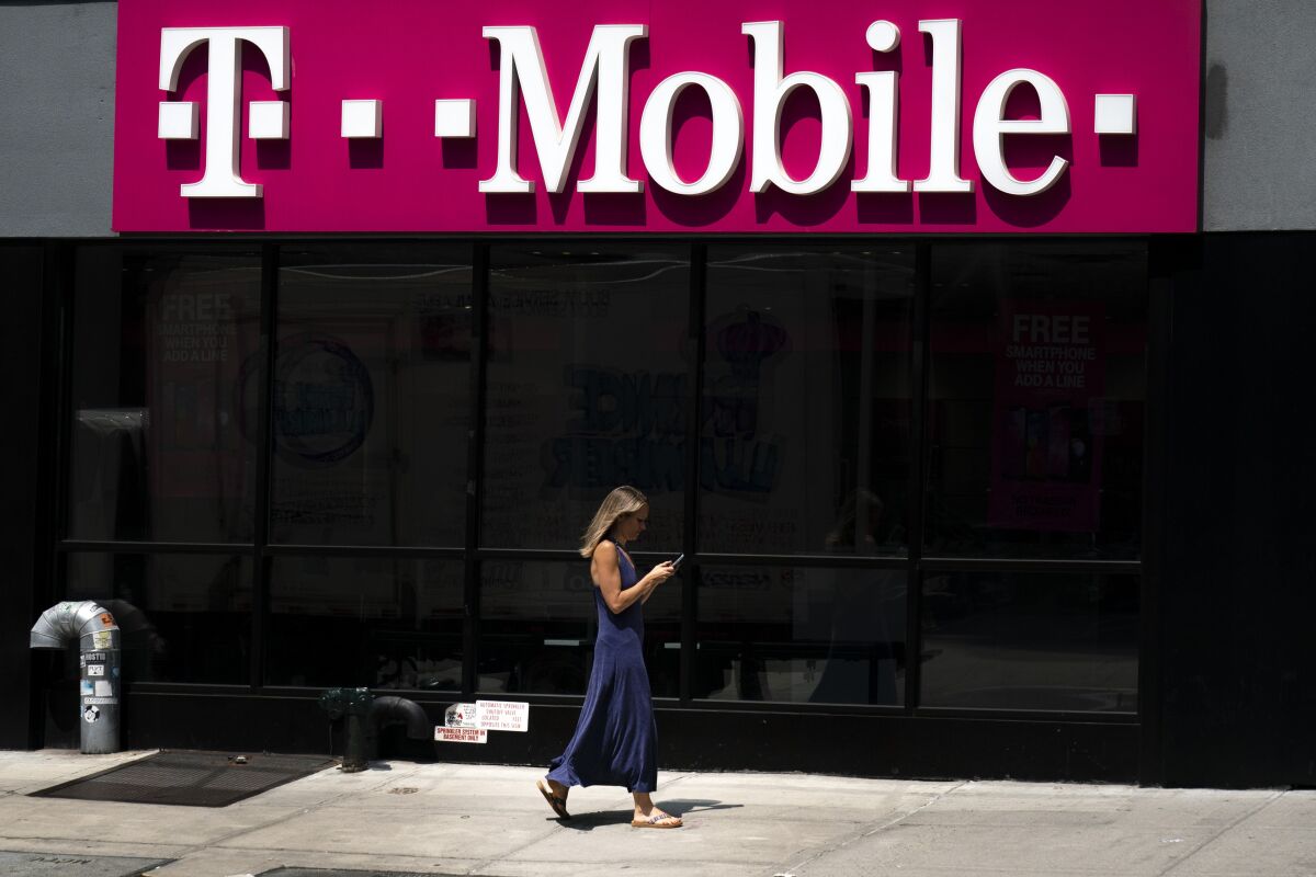 A woman looks at her phone as she walks by a T-Mobile store
