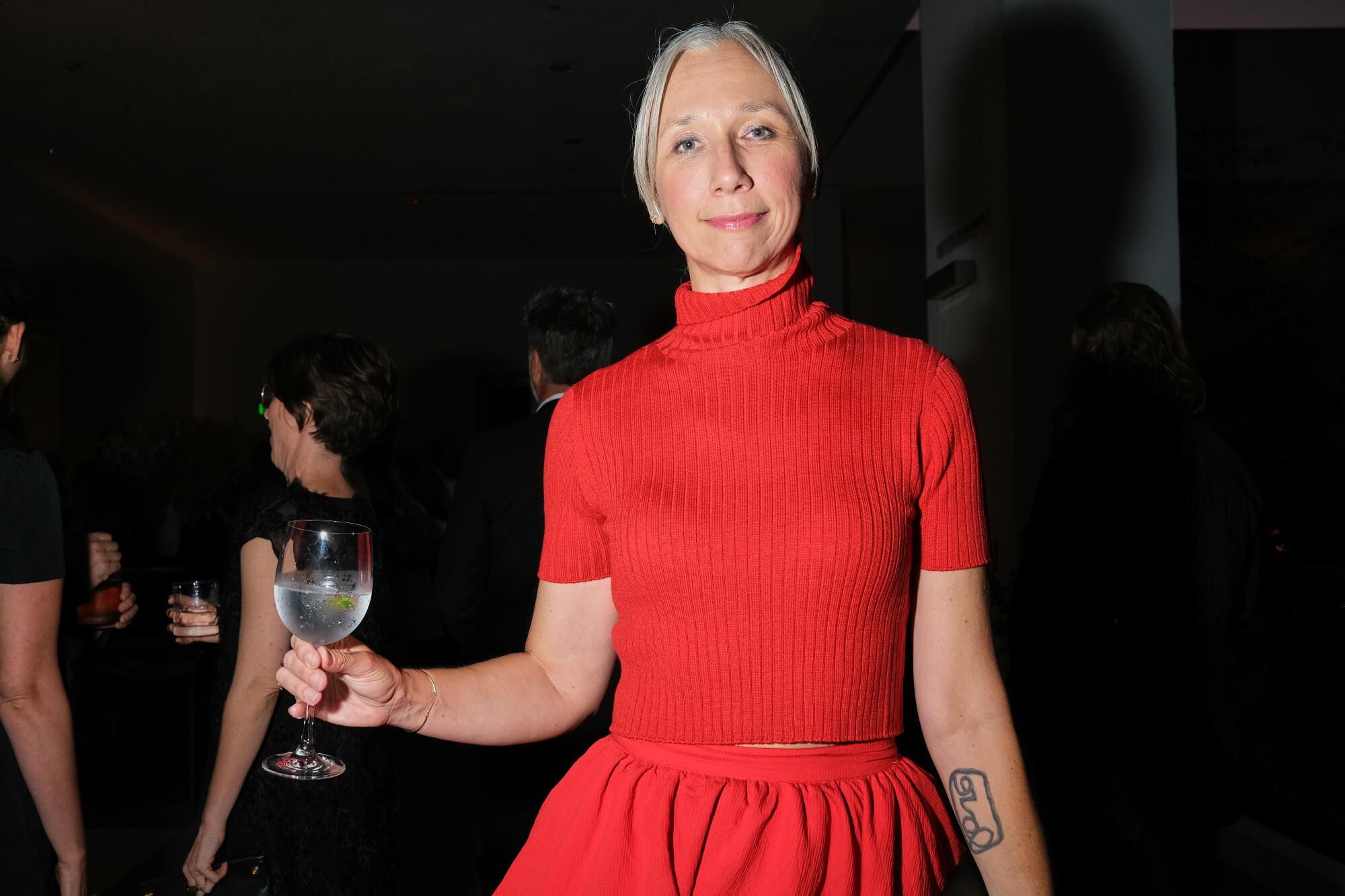 A woman dressed in all red clutches a wine glass at the gala.