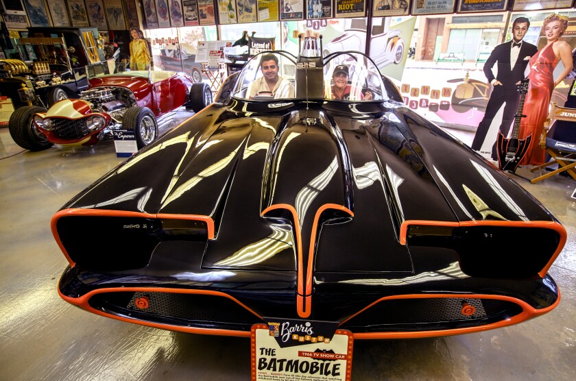 A man and his mother are photographed inside an exhibition replica of the Batmobile.
