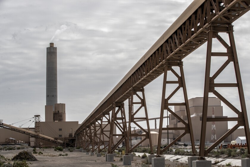 An industrial site with a smokestack, an elevated conveyor belt, scattered piles of coal.