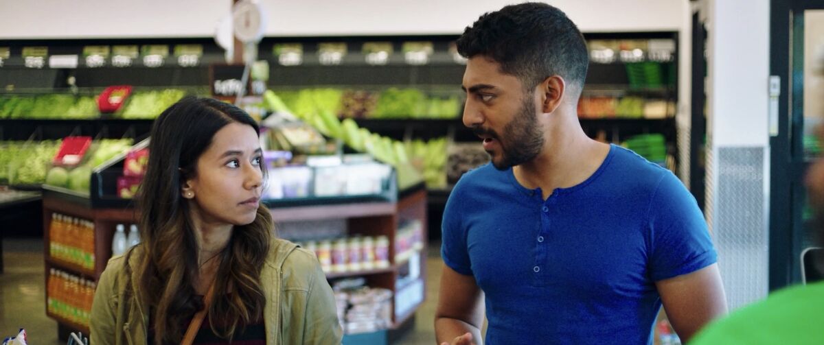 A man and a woman stand talking in the produce section of a grocery store.