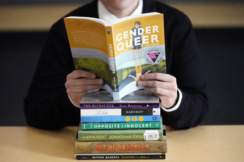 FILE - Amanda Darrow, director of youth, family and education programs at the Utah Pride Center, poses with books that have been the subject of complaints from parents in recent weeks on Thursday, Dec. 16, 2021, in Salt Lake City. A judge in Virginia dismissed a lawsuit Tuesday, Aug. 30, 2022, that sought to declare two books as obscene for children and to restrict their distribution to minors, including by booksellers and libraries. The books in question were “Gender Queer: A Memoir” by Maia Kobabe and “A Court of Mist and Fury” by Sarah J. Maas. (AP Photo/Rick Bowmer)