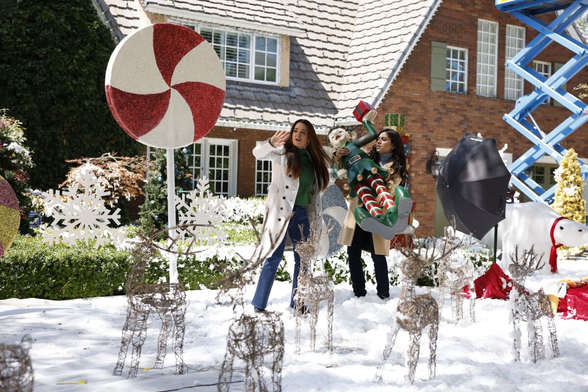 Two women place large Christmas decorations in a snowy yard.