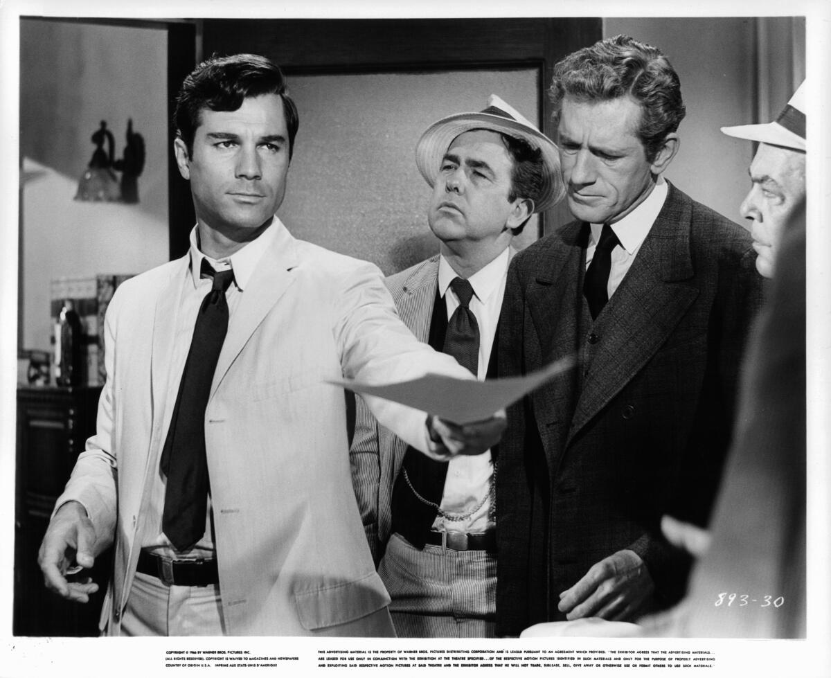 A man in a suit offers documents as three other men watch in a scene from the 1967 film "A Covenant With Death."