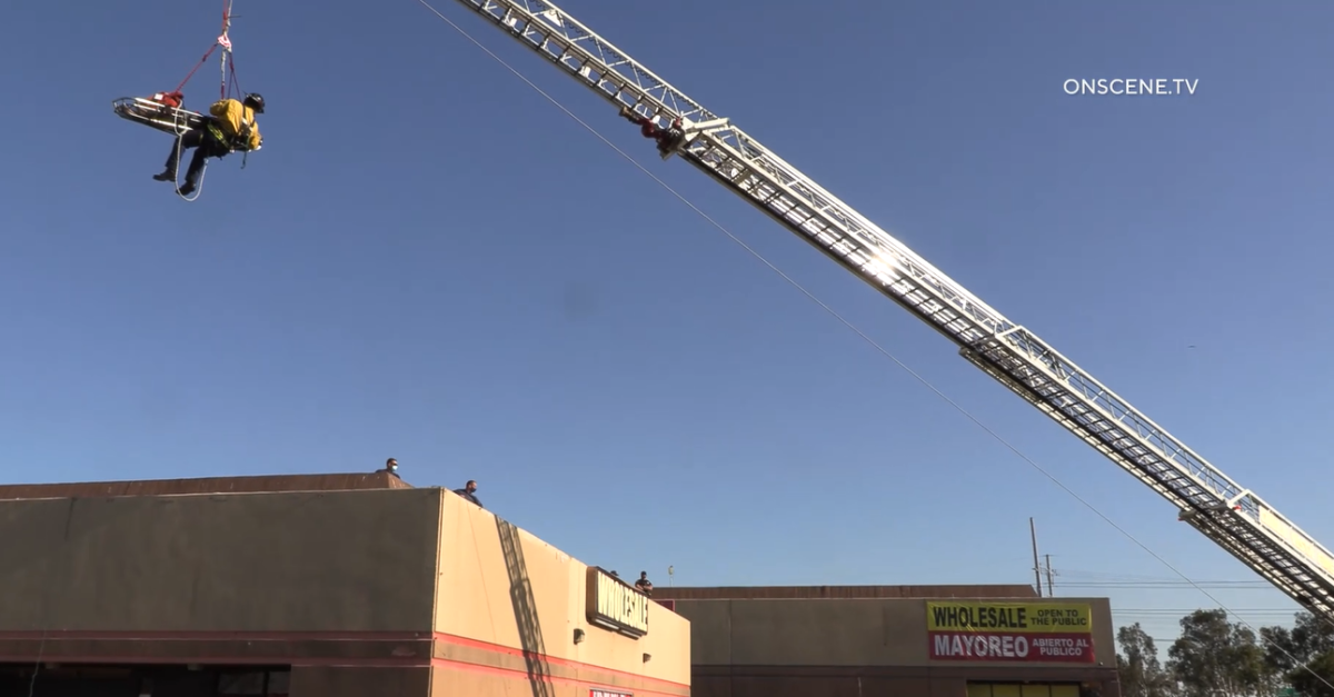 A ladder truck is used to lift a firefighter and a man from a roof.