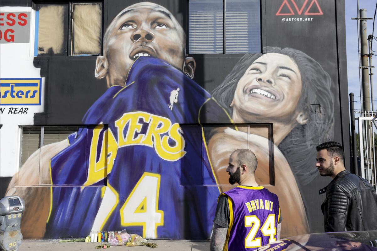 Two men stand in front of a mural honoring Kobe Bryant and his daughter Gianna outside of VEM Exotic Rentals.