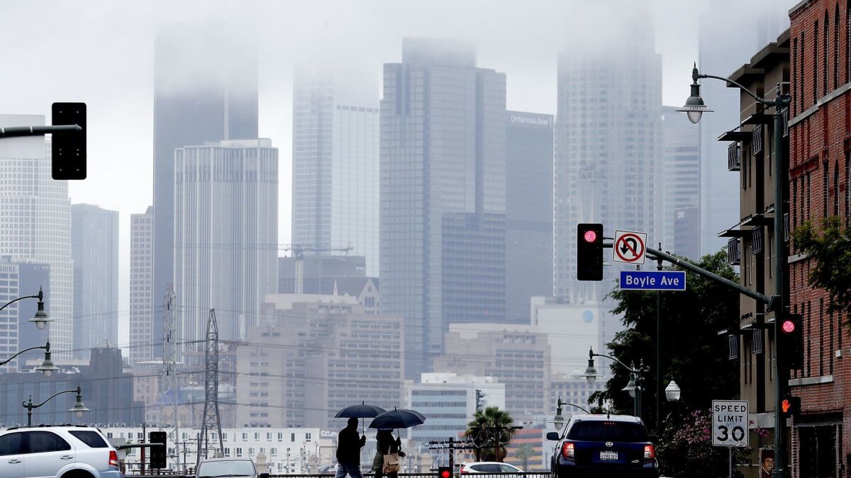 Pedestrians cross First Street in Boyle Heights as rain clouds partially obscure the downtown L.A. skyline on March 6.
