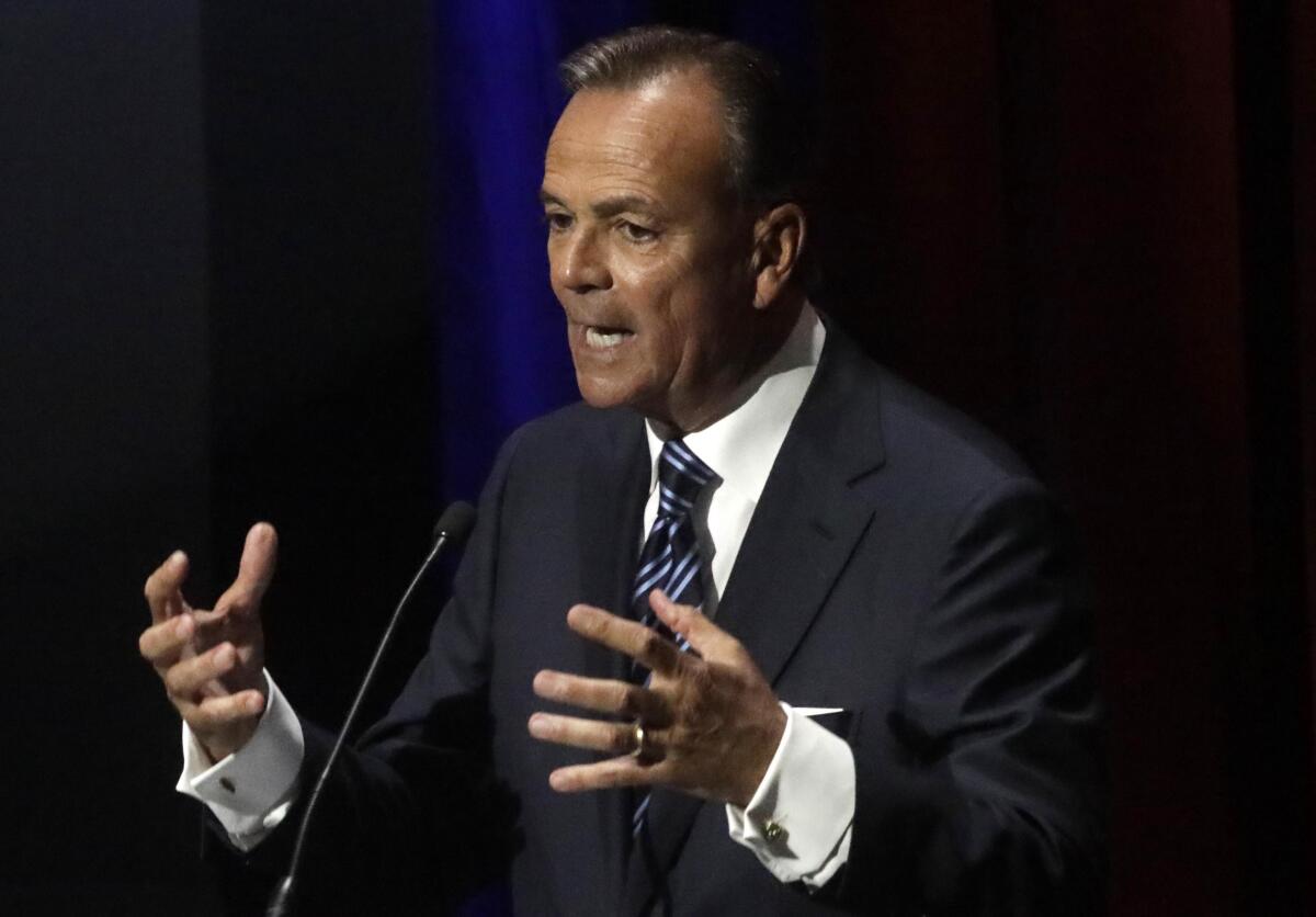 Rick Caruso holds up his hands while speaking at a microphone