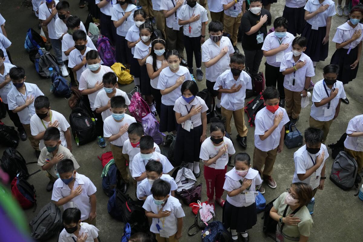 Masked students hold a hand over their heart and attend a flag raising ceremony.