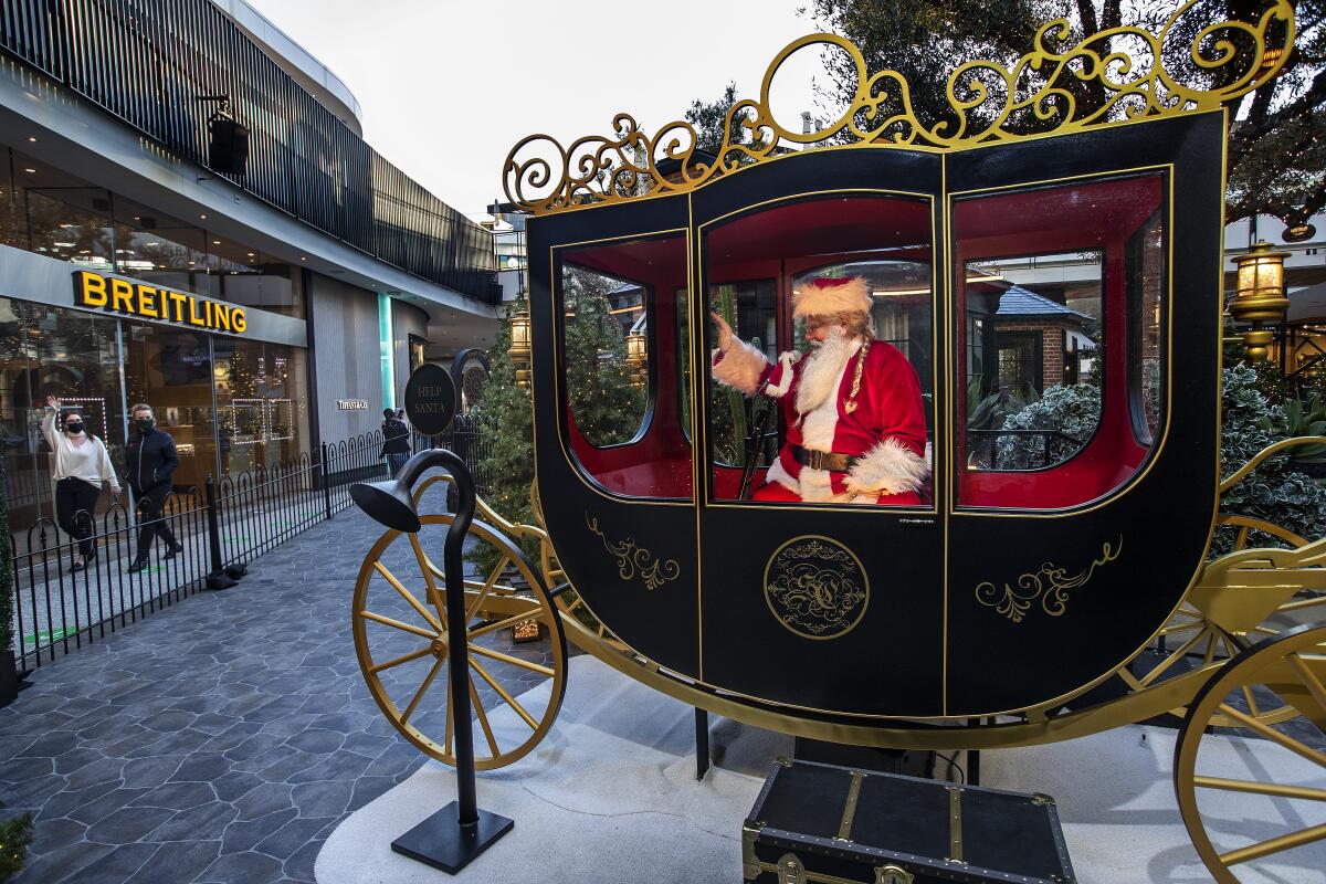 Santa Claus waves as he sits inside an ornate carriage at a shopping mall.