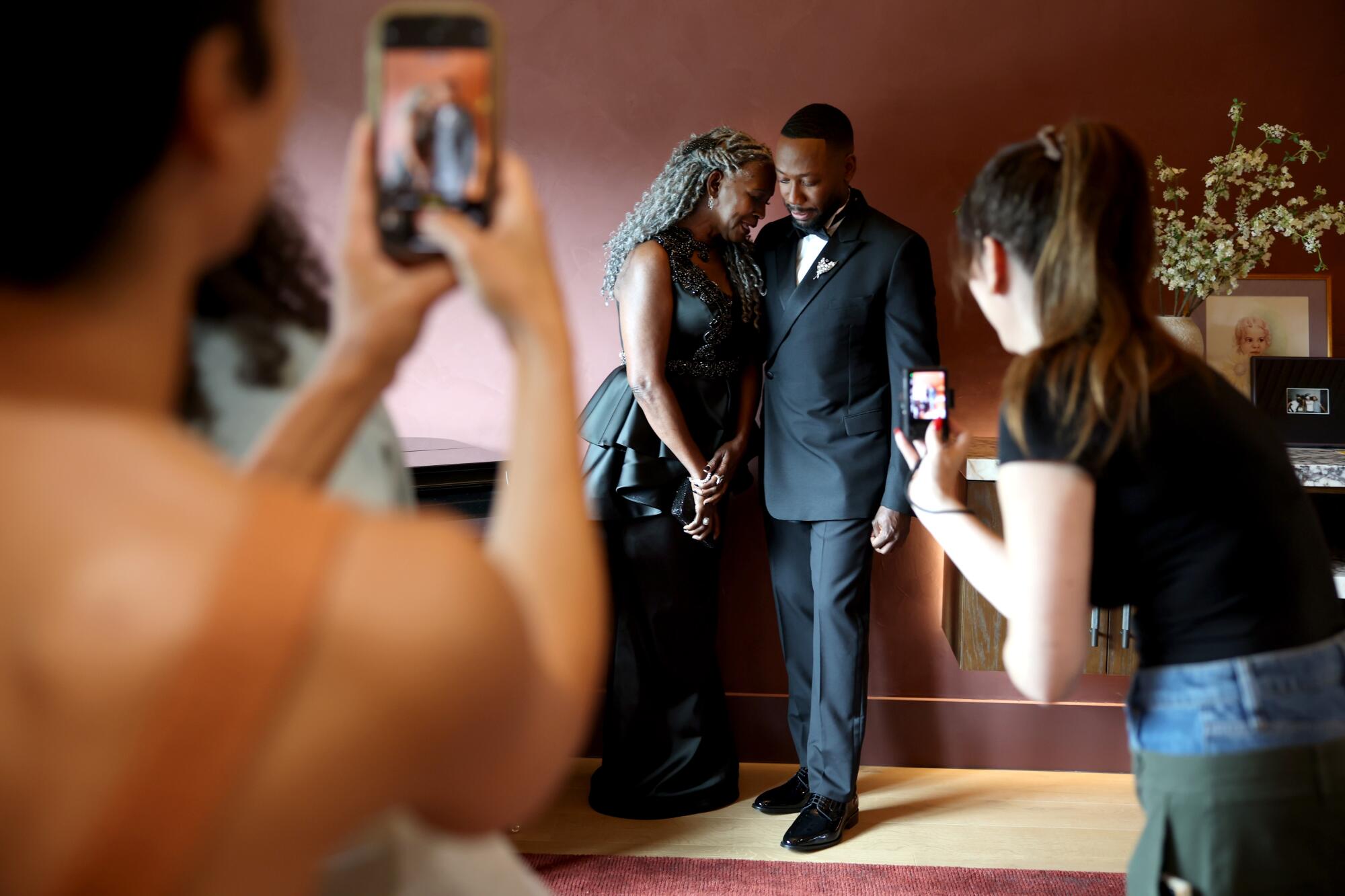 A woman in a dark dress and man in a tuxedo pose for photos.