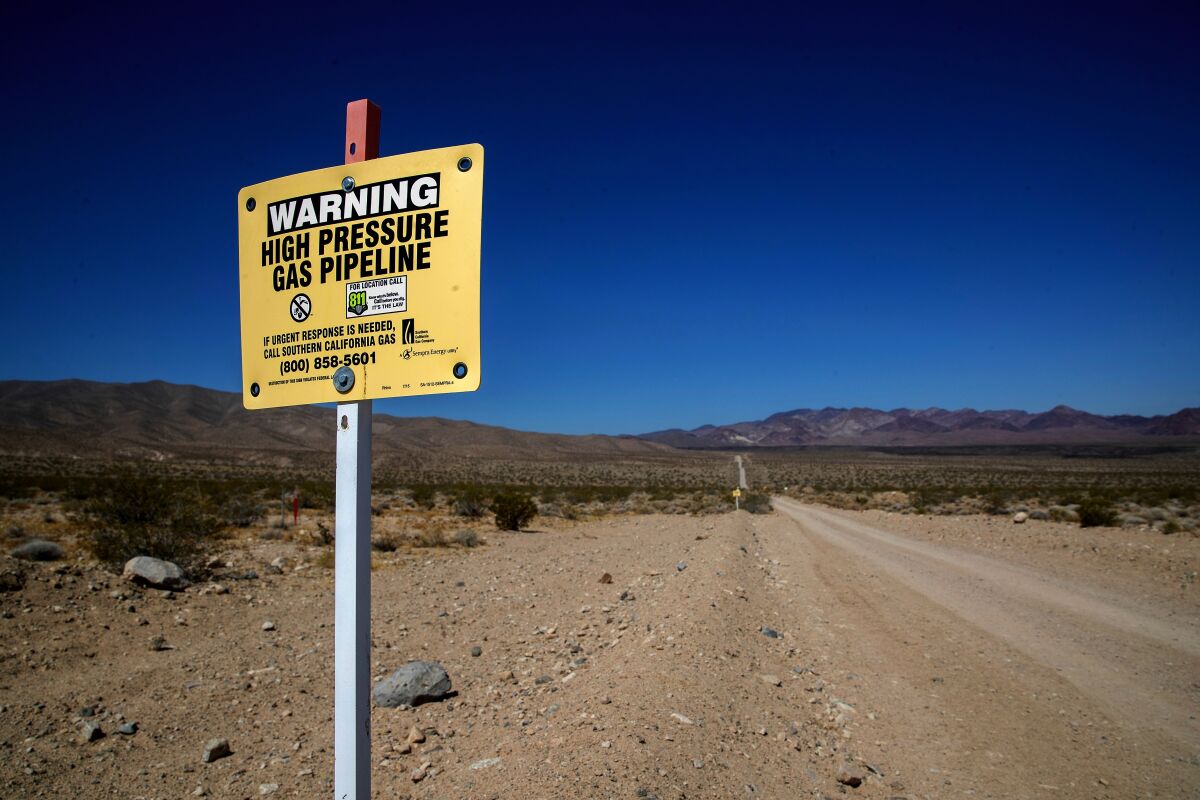 A sign next to a dirt road reads "Warning: High pressure gas pipeline."