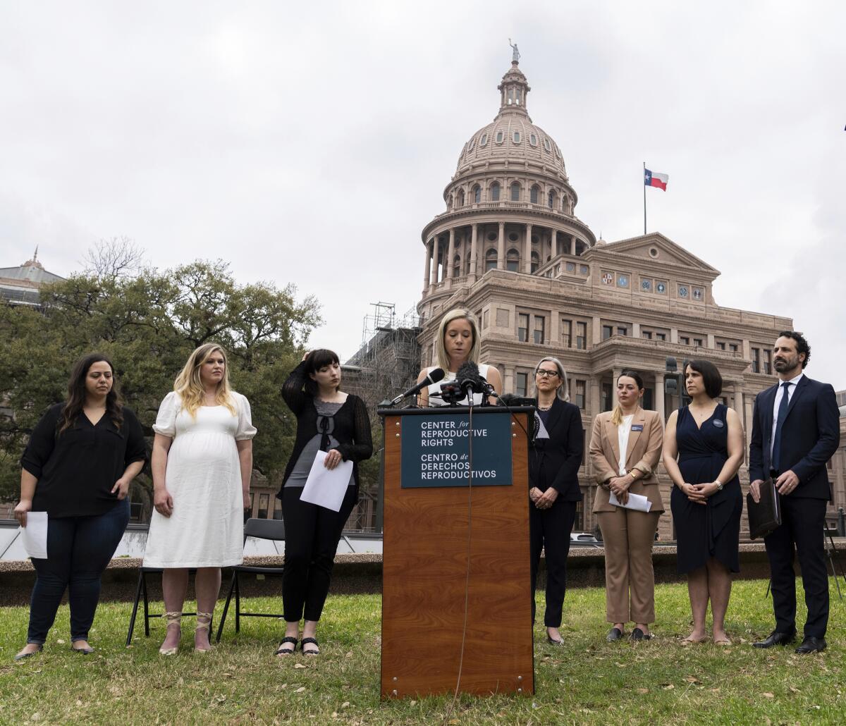 Amanda Zurawski speaks in front of the Texas Capitol while several people stand behind and on either side of her.