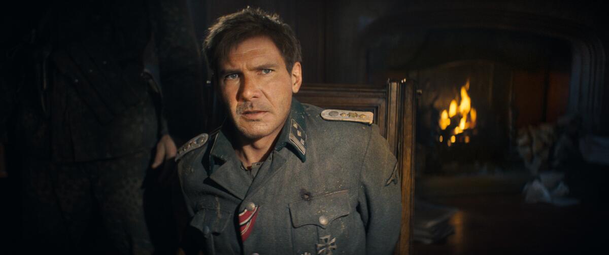 A seated, de-aged Harrison Ford in a military uniform, a fire burning in a fireplace behind him