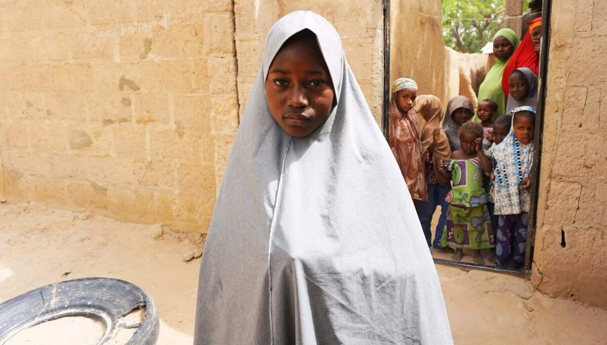Hassana Mohammed, 13, who scaled a fence to escape a suspected Boko Haram attack on her school, stands outside her home in Dapchi, Nigeria.