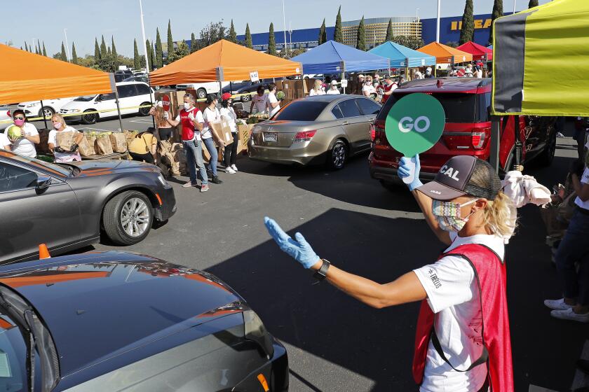 Volunteer Kelly Evans, right, directs drivers forward during a drive-thru giveaway at IKEA to help provide emergency food boxes filled with essential staples such as rice, beans, pasta and fresh produce to 1,200 low-income families in Costa Mesa on Thursday, April 23, 2020. IKEA, Community Action Partnership, OC Foodbank and Costa Mesa Councilmembers Arlis Reynolds and Andrea Marr helped coordinate this effort.