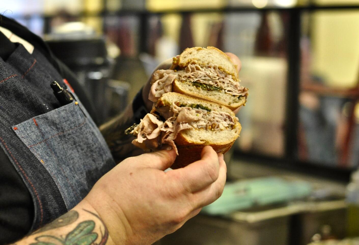 Bruce Kalman, the chef-owner of Knead & Co., holds one of his porchetta dip sandwiches at his new pasta bar in Grand Central Market.