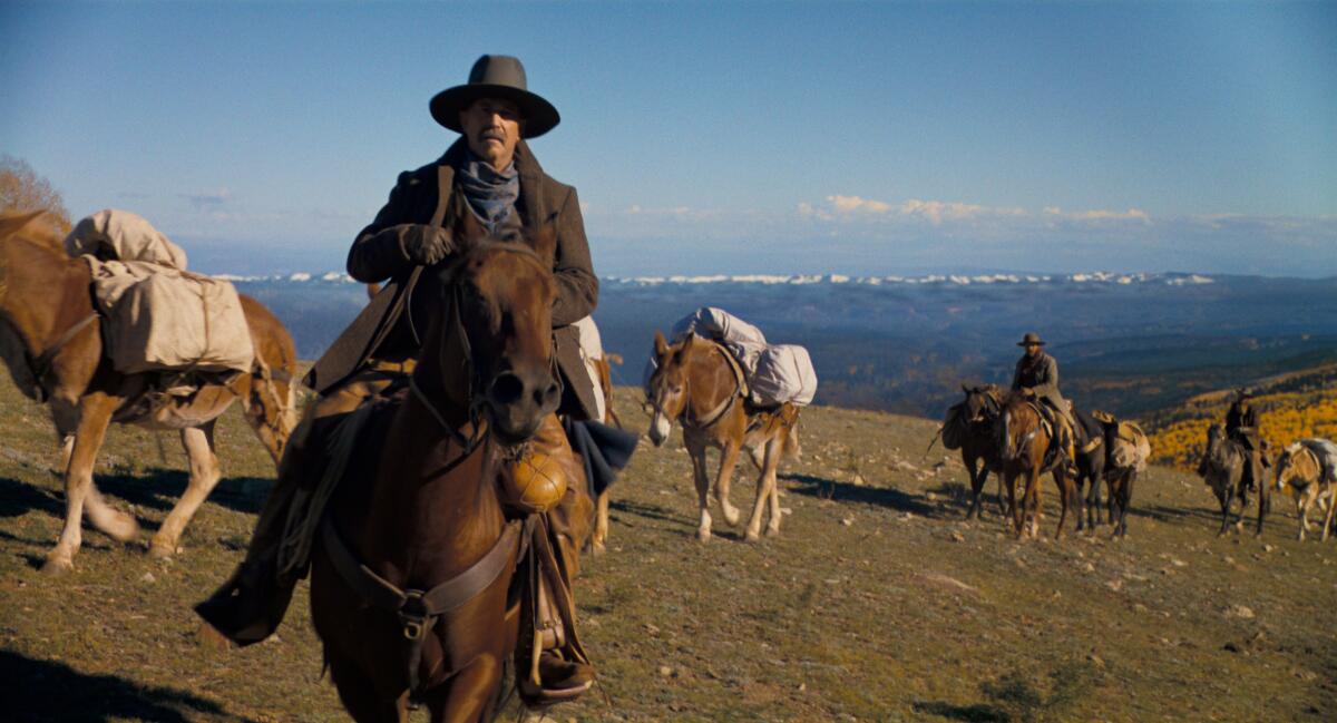 A man rides a horse on a mountain range, followed by pack horses.