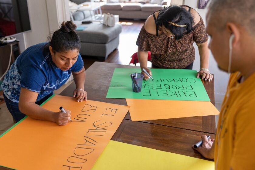 Marta Peinados, Rosa Flores, y Cesar Fuentes preparan carteles para la Cumbre de las Americas, en su hogar en Los Angeles.