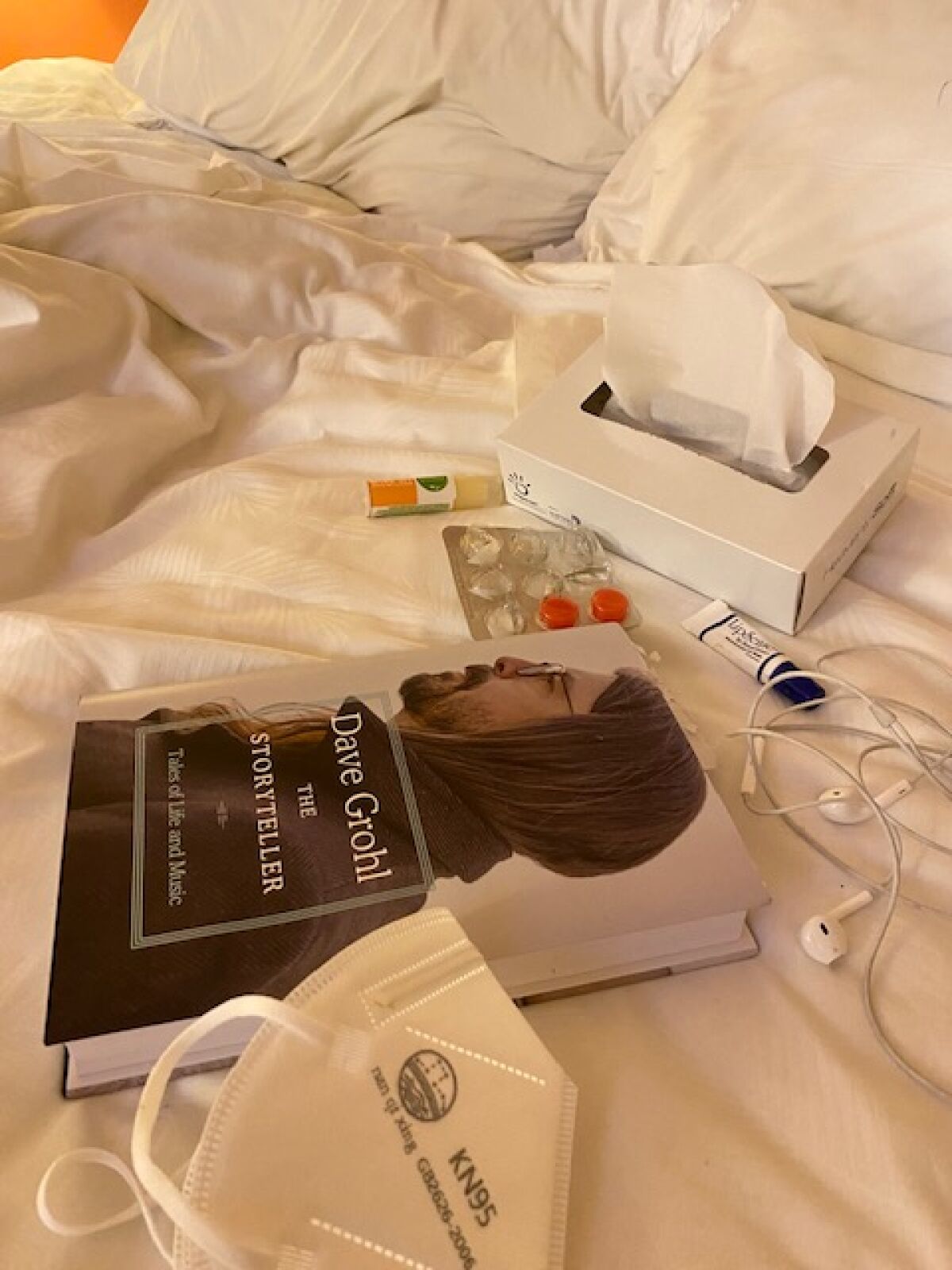 Cough drops, tissues, KN95 mask and the book "Dave Grohl: The Story Teller" on an unmade bed.