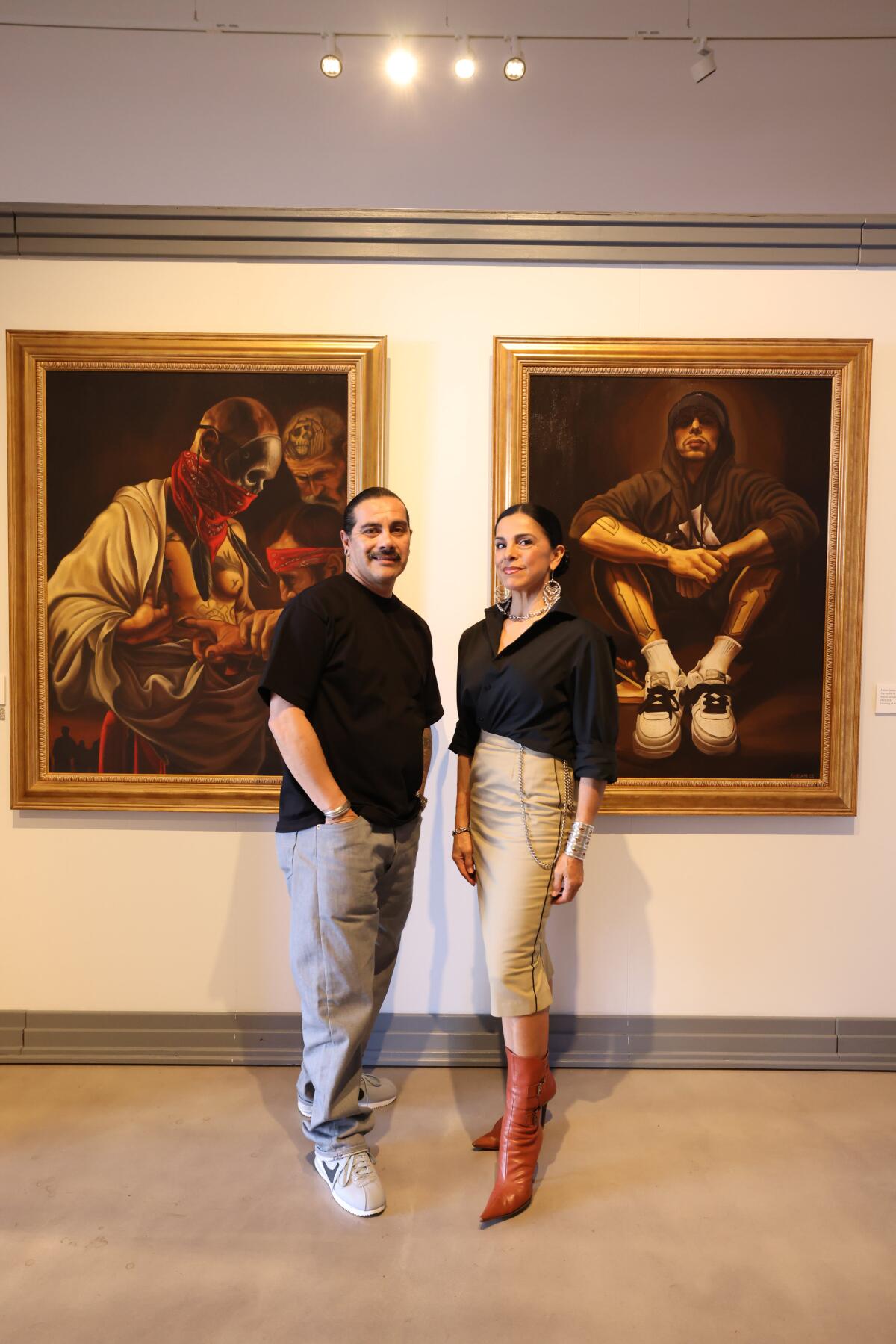 A man and woman stand in front of two paintings of people.