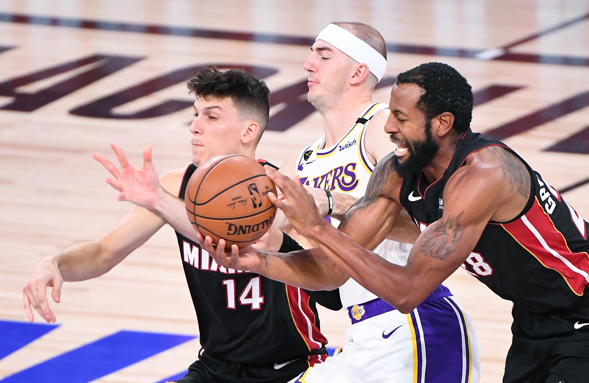 Lakers guard Alex Caruso is sandwiched by Miami's Tyler Herro, left, and Andre Iguodala while battling for aloose ball.