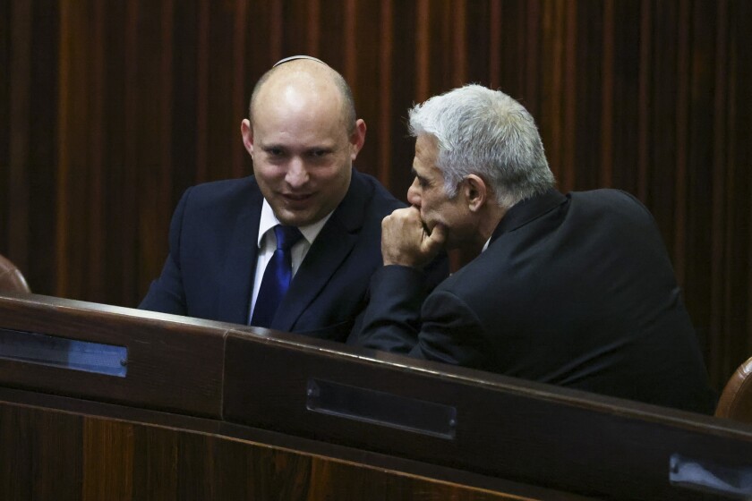 Yamina party leader Naftali Bennett, left, smiles as he speaks to Yesh Atid party leader Yair Lapid during a special session of the Knesset, whereby Israeli lawmakers elect a new president, at the plenum in the Knesset, Israel's parliament, in Jerusalem on Wednesday, June 2, 2021. (Ronen Zvulun/Pool Photo via AP)