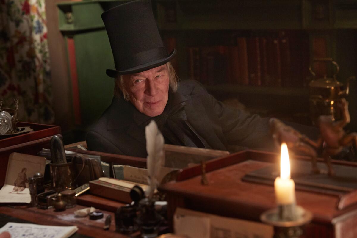 A man in a top hat sits near a wooden desk that has a quill pen in an ink pot and the stub of a burning candle.
