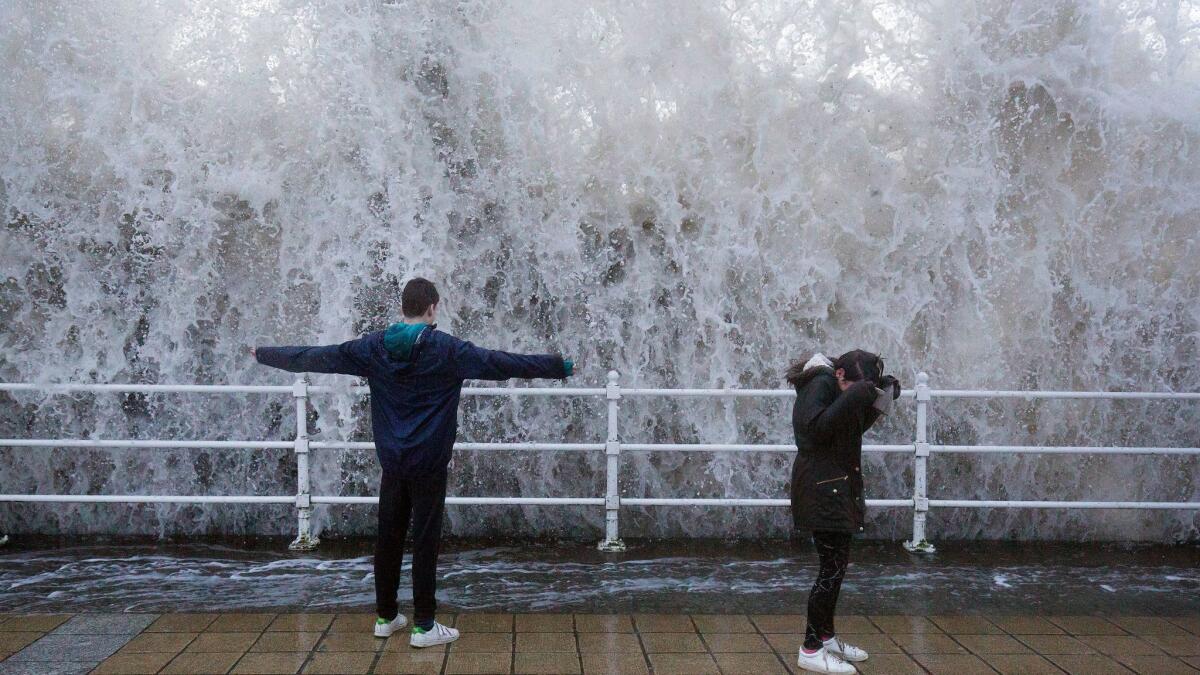 Children stand on the seafront as storm-driven waves crash over the seawall in Aberystwyth in western Wales on Jan. 3.