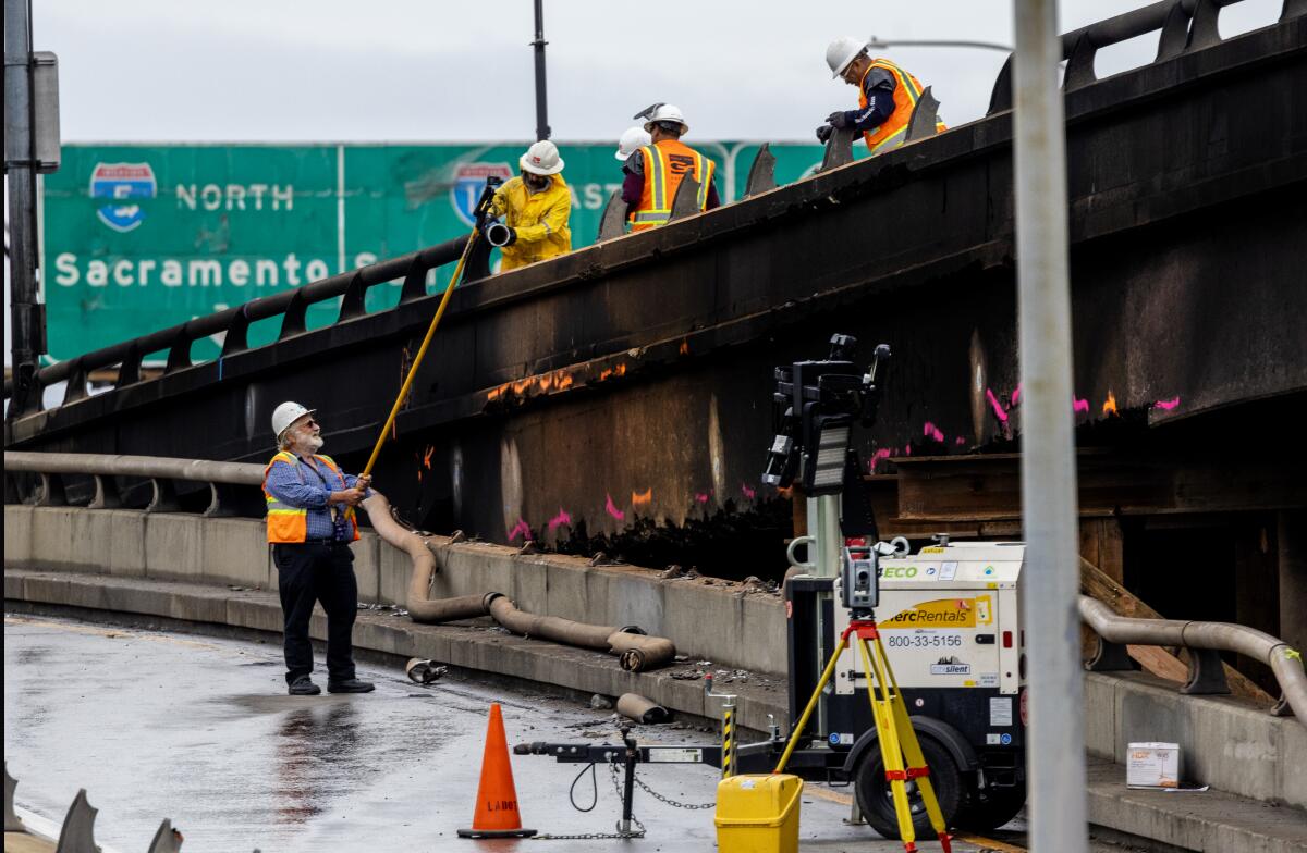 Construction workers take measurements along the burned portion of the 10 Freeway above 14th Street at Alameda.