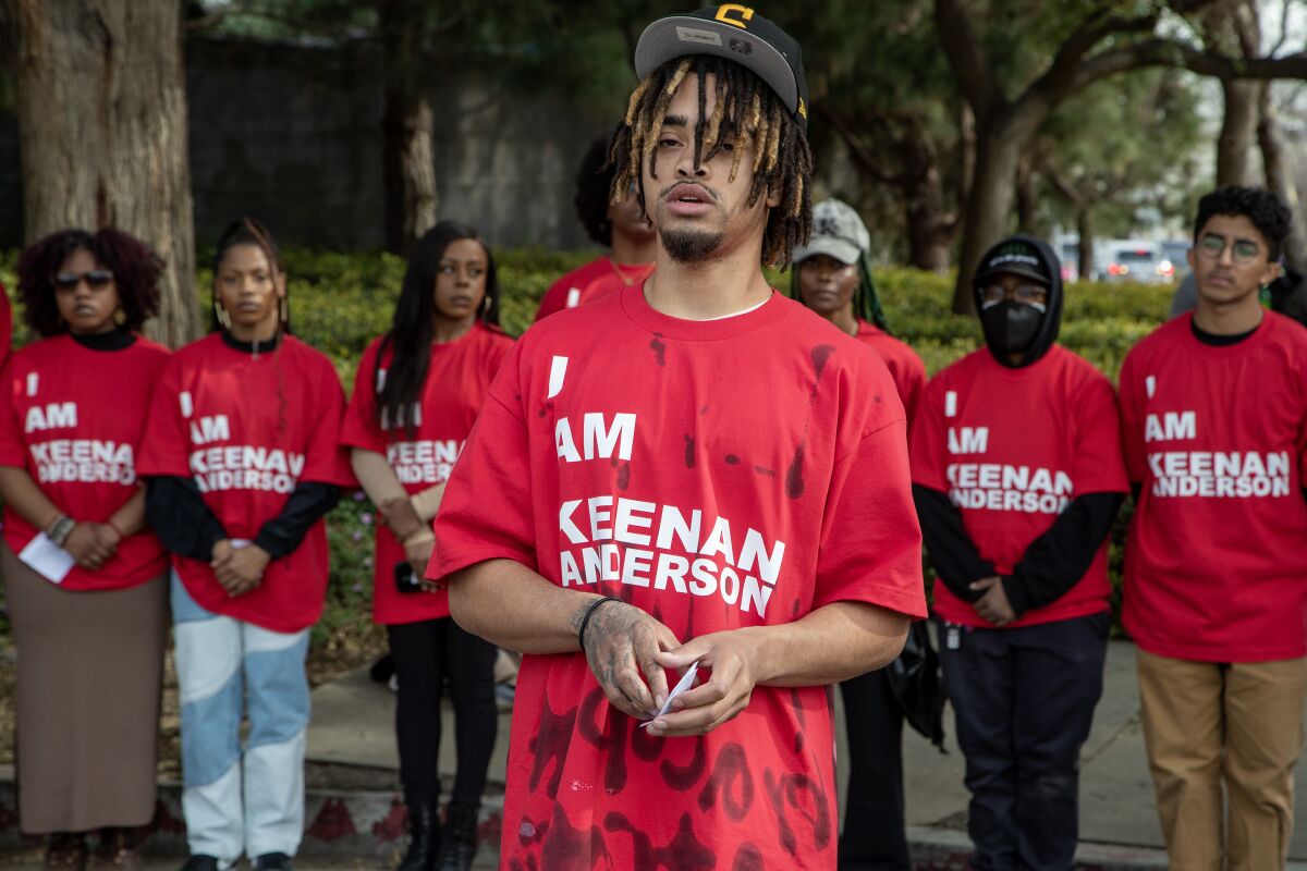 A man in a red T-shirt saying "I Am Keenan Anderson" stands in front of others in red T-shirts saying the same thing.