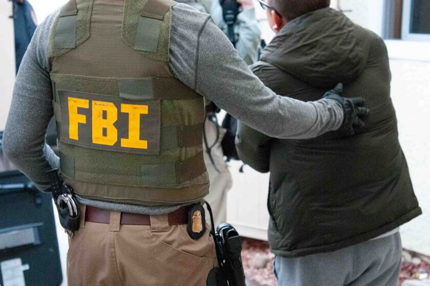 An FBI special agent escorts a suspect during a series of morning arrests Wednesday. Fourteen people are charged with operating a scam that exchanged fake iPhones from China for real ones at Apple stores in the U.S. and Canada.