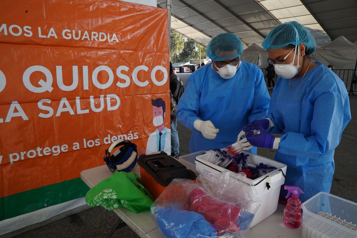 Two people in protective gear handle medical supplies at an outdoor table.