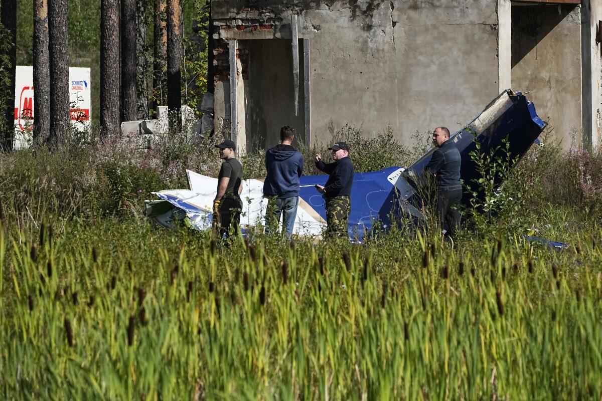 Russian servicemen inspect a part of a crashed private jet near the village of Kuzhenkino