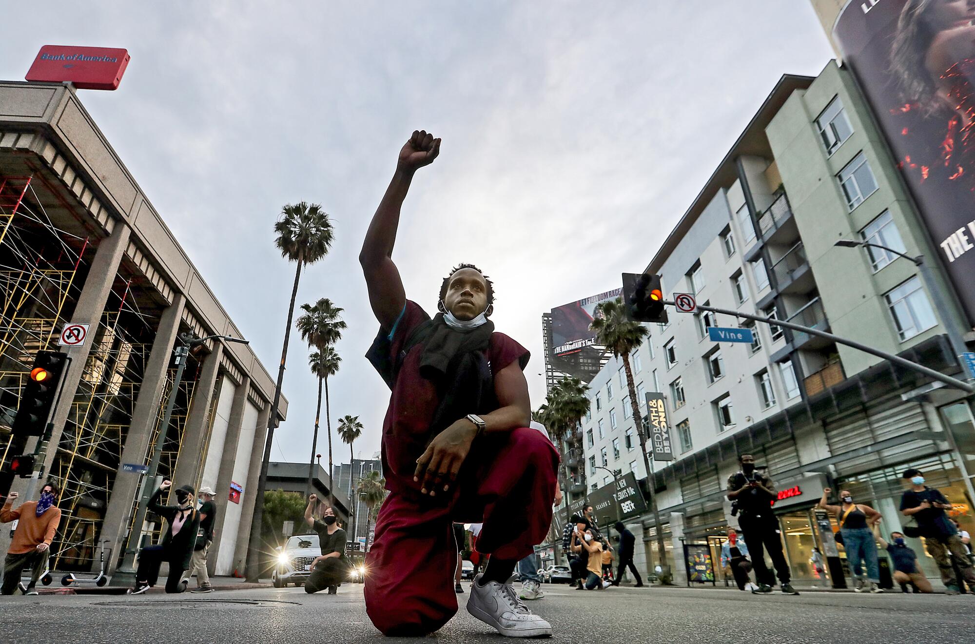 A man kneels in the intersection at Sunset and Vine, raising a fist.