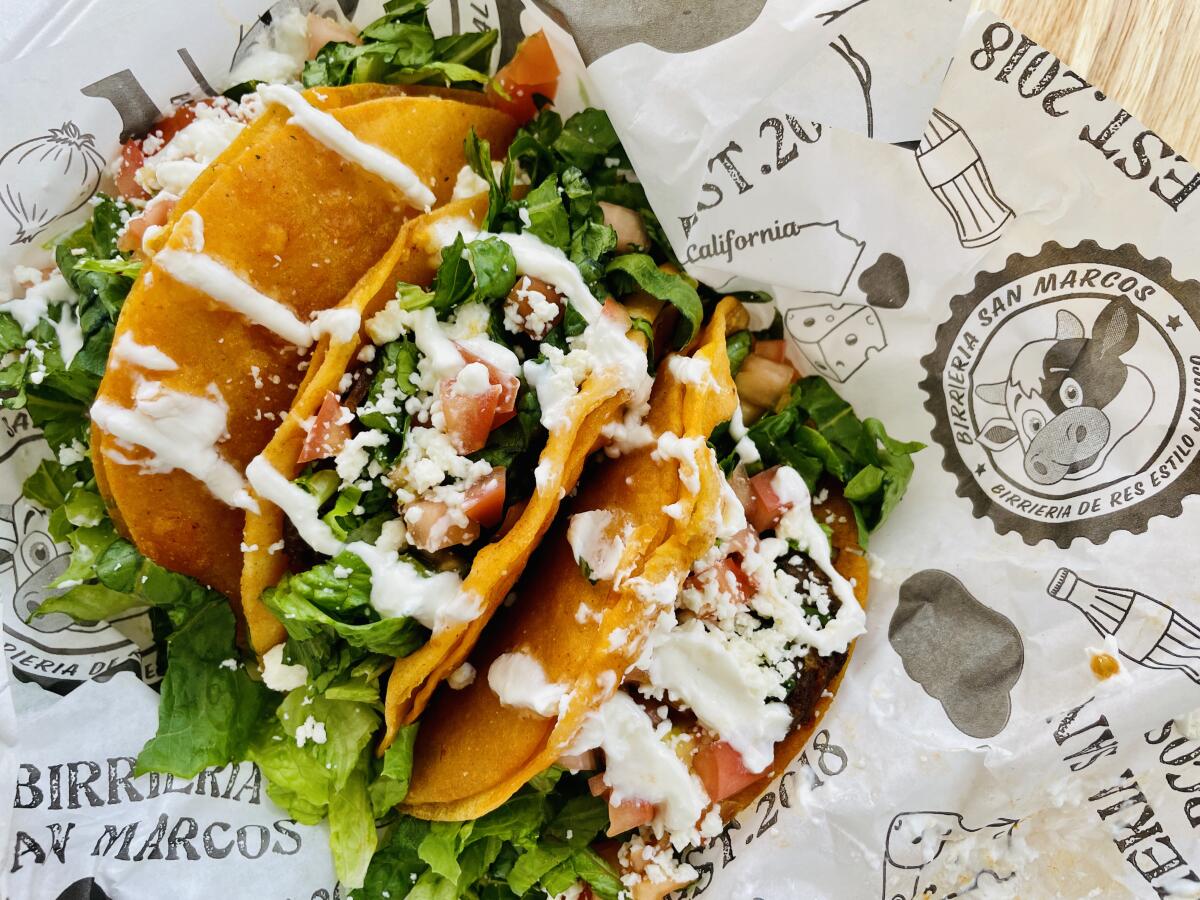 Three hard-shell tacos topped with lettuce, tomatoes, cheese and crema