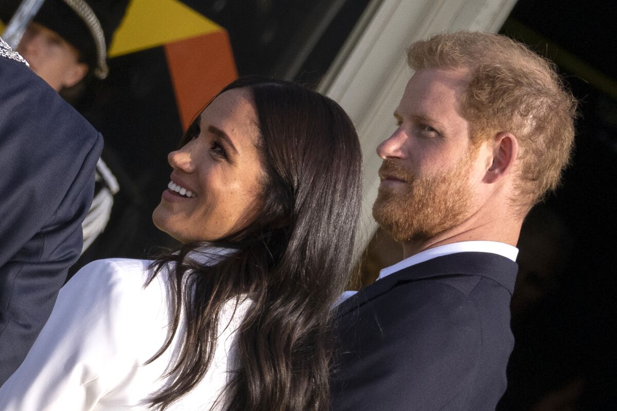 Prince Harry and Meghan Markle smile as they arrive at an event.