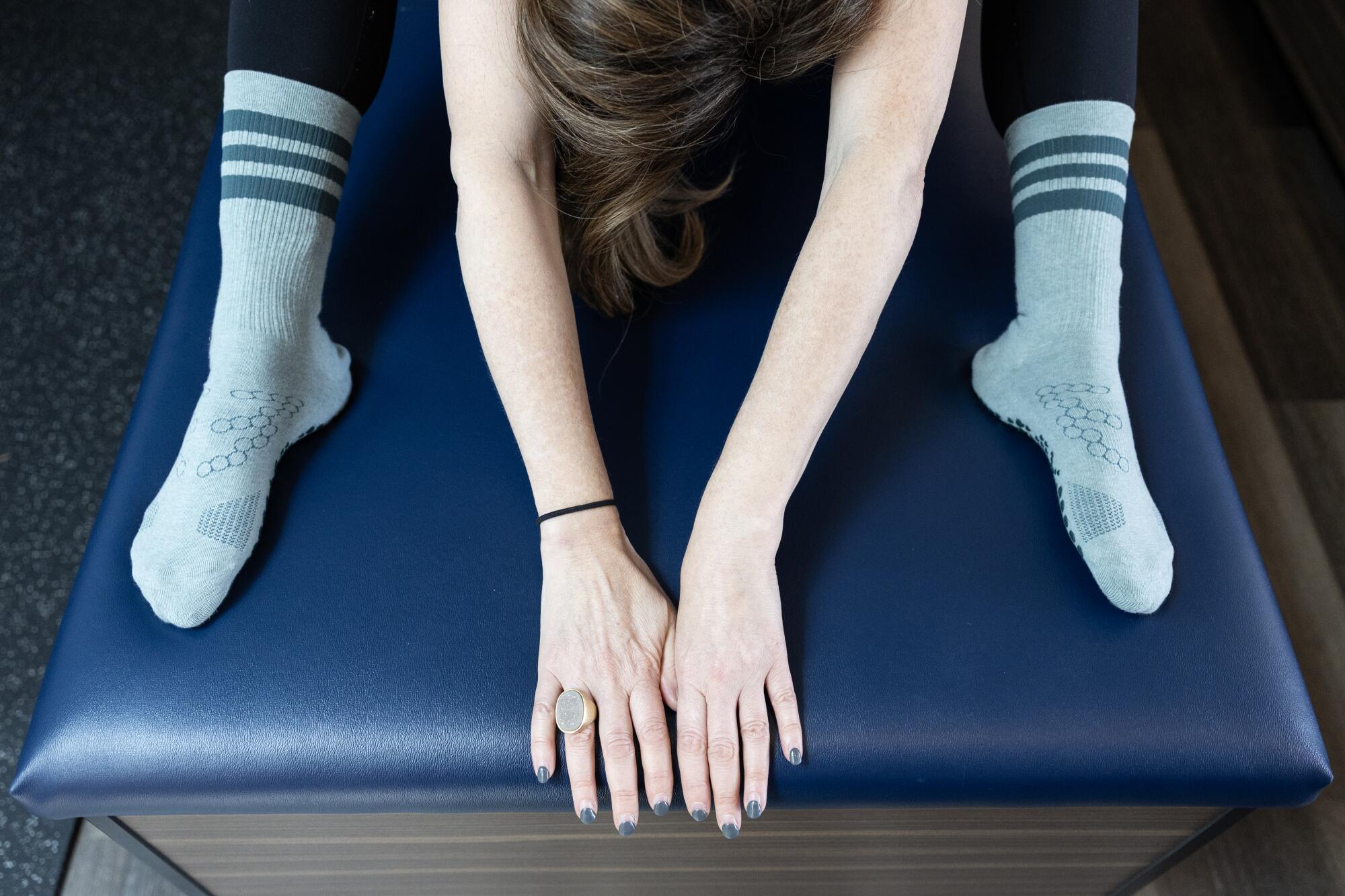 A woman performs a forward fold stretch on a massage table.
