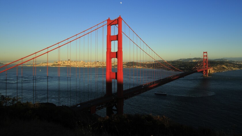 A ship passes under the Golden Gate Bridge, seen from the Marin Headlands side with San Francisco in the background