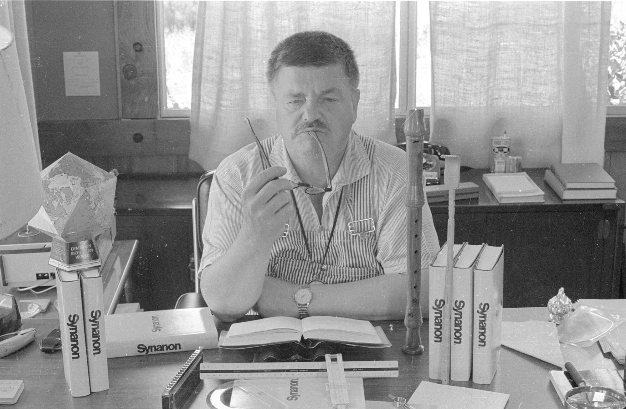 A man seated at a desk holding a pair of glasses.