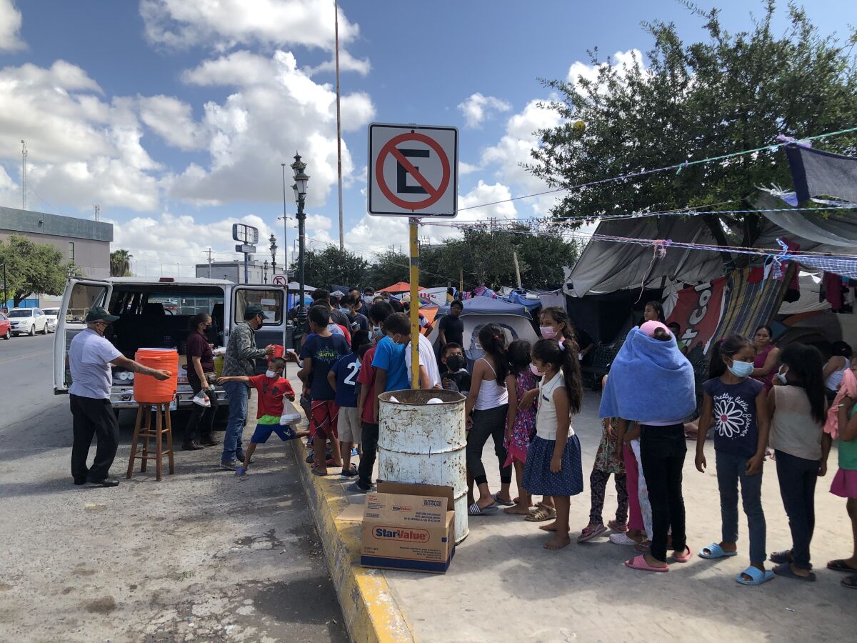 Migrants line up to receive food and water distributed by a Mexican minister at Plaza Las Americas migrant camp in Reynosa.