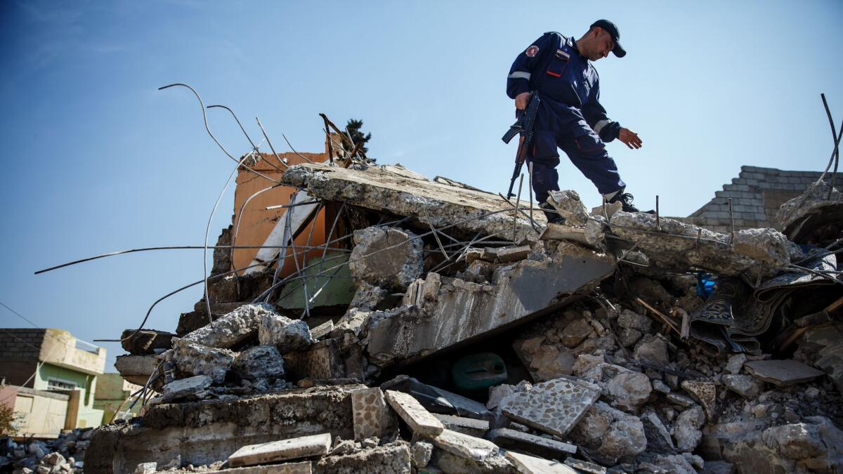 An Iraqi civil defense force member stands guard while work is done to remove the rubble and dead bodies from a home destroyed by a coalition air strike in the Jadidah neighborhood of Mosul on March 24, 2017. (Marcus Yam / Los Angeles Times)