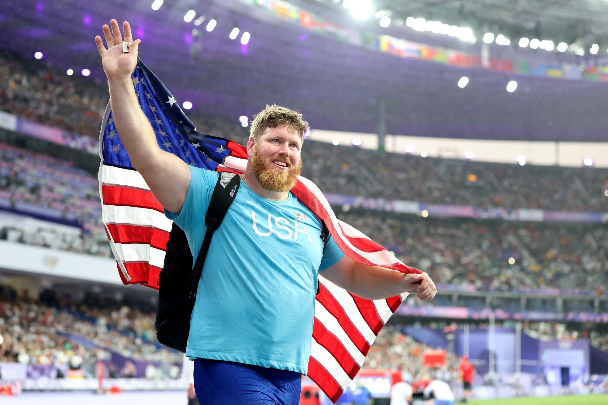 American Ryan Crouser is draped in a U.S. flag and waves in a stadium.