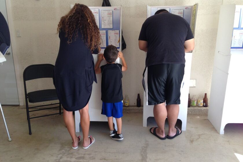 Gigi Modlin, left, with her son, Hayden Modlin looking, on, and Michael Roberts, right, vote in Mira Mesa Tuesday morning.