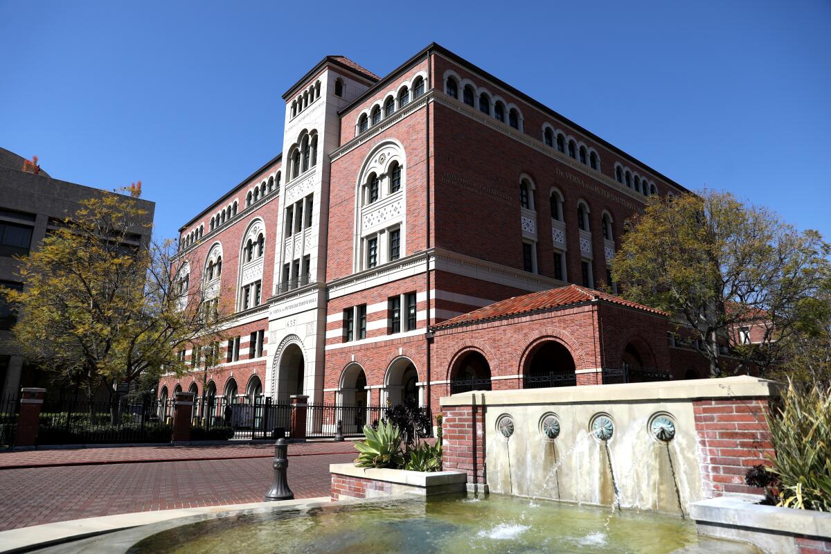 A large, red-brick university building with a fountain and cobblestone path in the foreground.