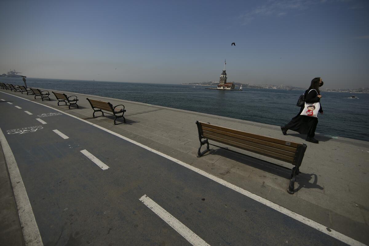 Backdropped by the Maiden's Tower a woman walks on a nearly deserted promenade by the Bosphorus Strait in Istanbul, Friday, April 30, 2021, on the first day of a tight lockdown to help protect from the spread of the coronavirus. Turkish security forces on Friday patrolled main streets and set up checkpoints at entry and exits points of cities, to enforce Turkey’s strictest COVID-19 lockdown to date. Still, many people were on the move as the government, desperate not to shut down the economy completely, kept some sectors exempt from the restrictions. (AP Photo/Emrah Gurel)